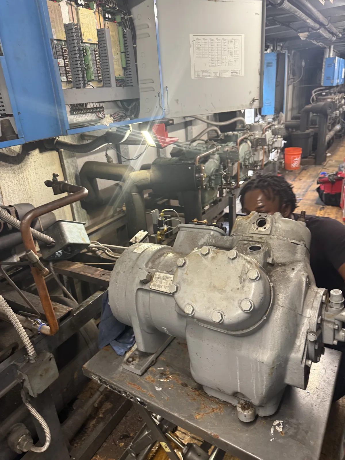 A Vice Mechanical technician rebuilding a commercial refrigeration compressor in a machine room